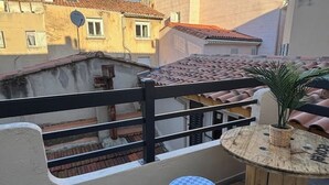 Ein Balkon mit einem karierten Tisch und einem Blumentopf, mit Blick auf ein Gebäude mit einem Ziegeldach.