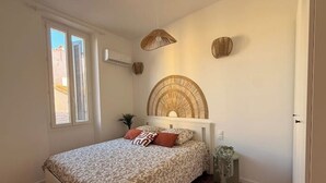Ein Schlafzimmer mit einem Bett, einem Fenster mit Fensterläden, einer Wandleuchte und einem Wanddekor.
