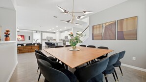 A modern dining area with a wooden table and black upholstered chairs, a central plant, and abstract wall art. - 9BR house sleeps 24 with pool table (Kissimmee)