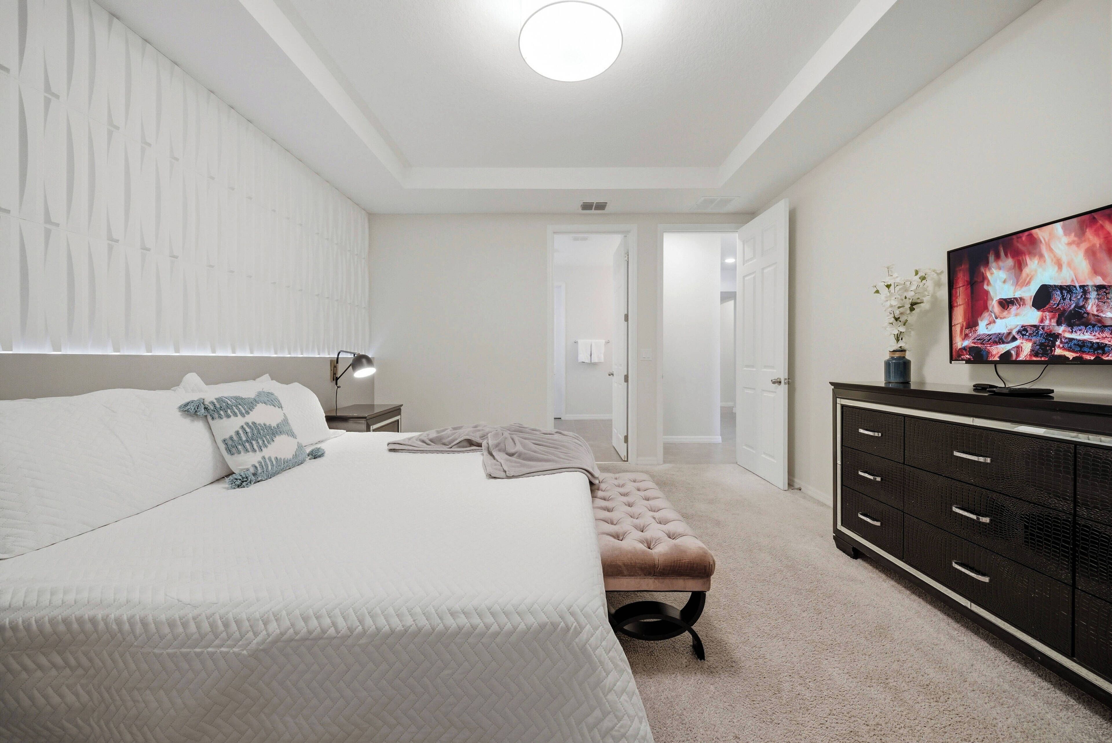 A bedroom with a large bed, a bedside table, a TV, and a dresser.