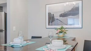 A dining area with a long table set for two, a framed artwork above, and a small plant on the table.