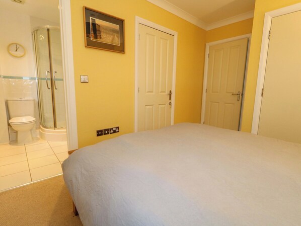 A bedroom with a bed, a bathroom with a shower, toilet, and a clock.