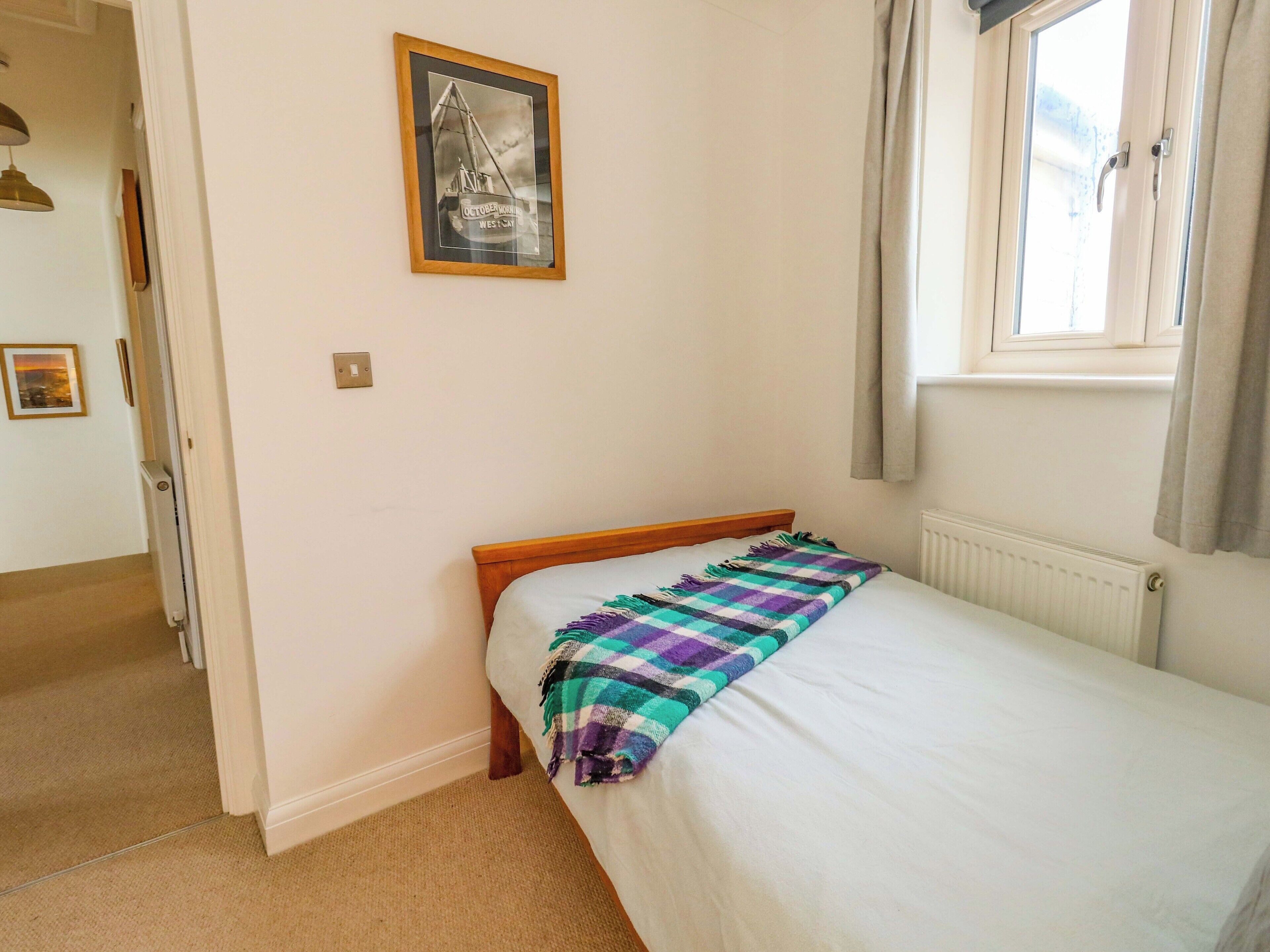 Une chambre avec un lit simple, une fenêtre avec des rideaux, un radiateur et un tableau encadré au mur.