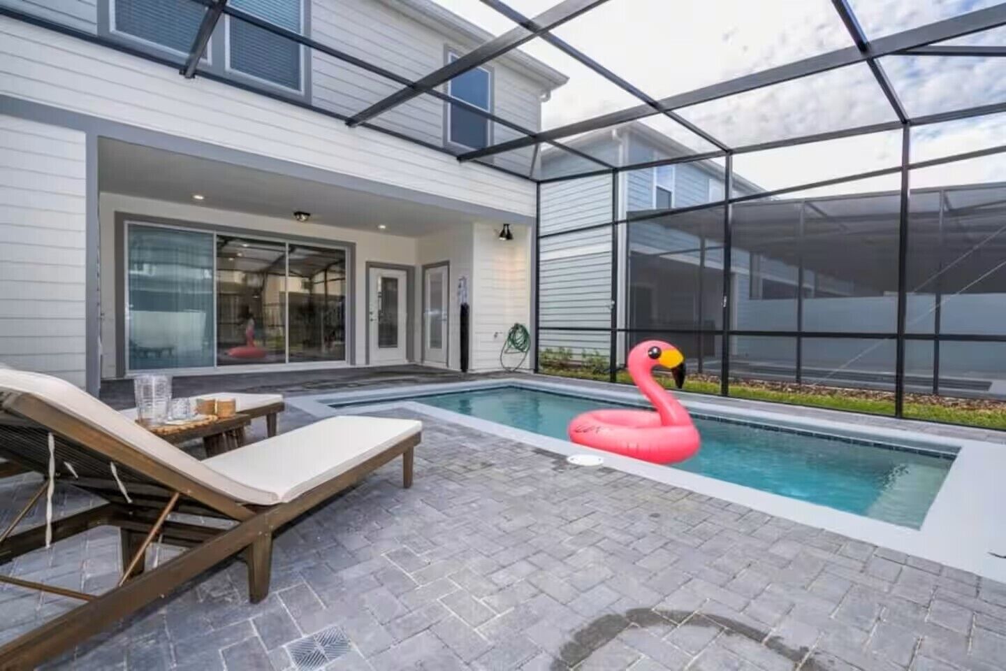Una casa moderna con un porche de vidrio, una piscina y un flotador con forma de flamenco.