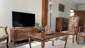 Een woonkamer met een houten kast, een televisie, een tafel met decoratieve objecten, twee fauteuils, een vloerlamp en een kast met deuren.