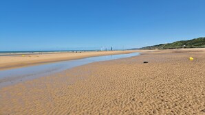 Een breed zandstrand met zachte golven, een heldere blauwe lucht en een verre blik op heuvels.