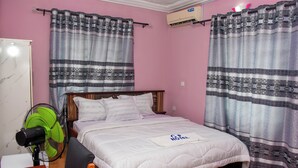 Ein Hotelzimmer mit einem Bett, einem Nachttisch mit Fernbedienung, einem grünen Ventilator und Vorhängen.