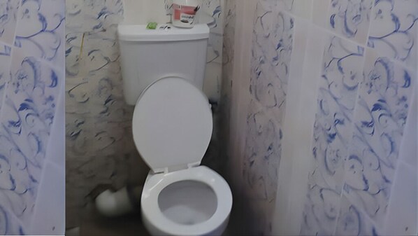 A bathroom with a toilet, a white toilet paper holder, and a roll of toilet paper on the wall.