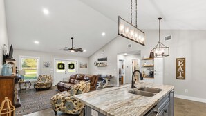Un vaste espace de vie comprenant une grande cuisine avec un îlot central, des meubles en cuir et une décoration d’inspiration rustique.
