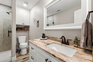 Une salle de bain avec des toilettes blanches, un lavabo doté d’un plan de travail en marbre et un grand miroir.