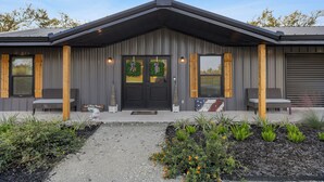 Un bâtiment moderne à la façade sombre, doté de piliers en bois et d’un porche à l’avant, aménagé avec des sièges.