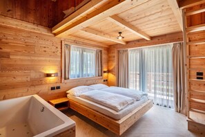 Ein Schlafzimmer einer Holzhütte mit einem großen Bett, einer Badewanne und zwei mit Vorhängen versehenen Fenstern.