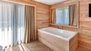 Een badkamer met houten lambrisering, een groot bad, een spiegel en gordijnen.