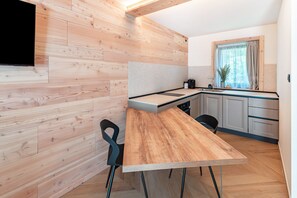 A modern kitchen with wooden cabinetry, a wooden dining table, and a black chair. - Noah Suites Neve Apartment with Mountain View, Private Terrace and Wi-Fi (Vigo di Fassa)