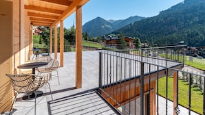 Een balkon met uitzicht op bergen, houten balken en buitenmeubilair.