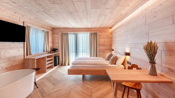Een moderne slaapkamer met houten vloer, een bed, bureau, stoel, televisie en een bad.