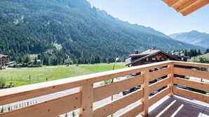 Ein Holzbalkon mit Blick auf eine gebirgige Landschaft, eine Straße und Gebäude in der Ferne.