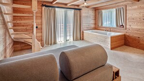 Ein Holzinnenraum mit Treppe, großem Fenster mit Vorhängen, einer Badewanne und einem Sofa.