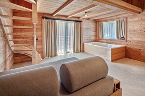 A wooden interior with a staircase, a large window with curtains, a bathtub, and a sofa. - Noah Suites Piuma Apartment with Mountain View, Shared Garden and Wi-Fi (Vigo di Fassa)
