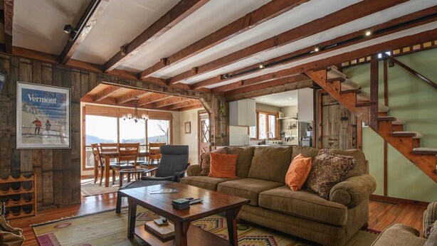 Un intérieur rustique avec des poutres apparentes, un coin salon confortable avec un canapé et une table basse, et un escalier menant à un niveau supérieur.