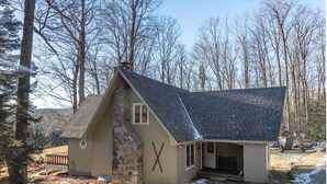 Une cabane rustique avec une façade en pierre, une grande cheminée et une véranda.