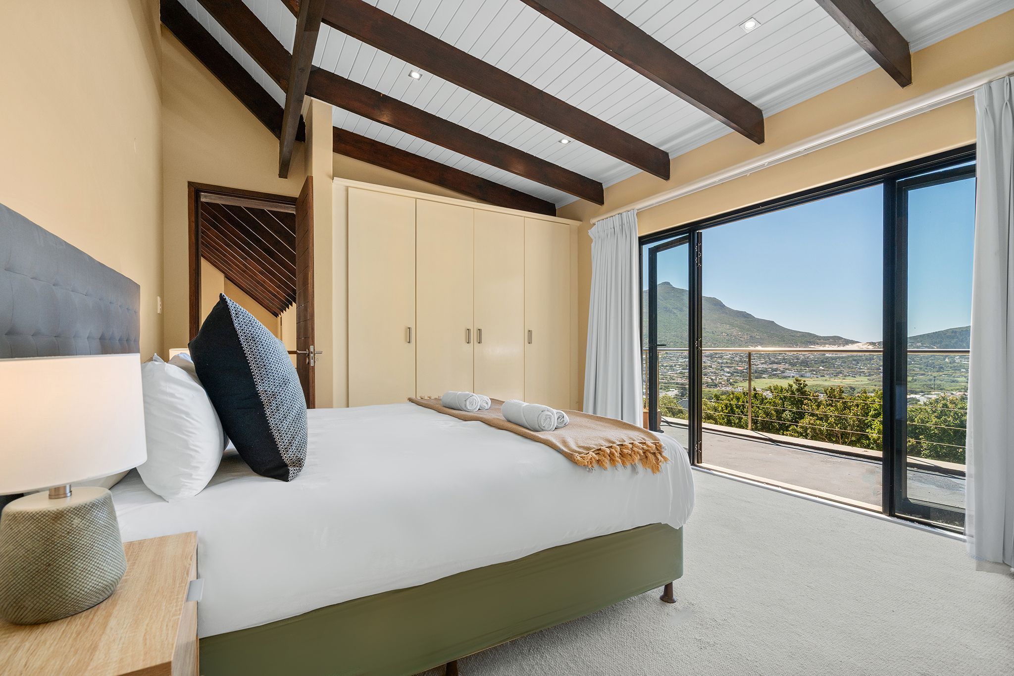 A bedroom with a large bed, a nightstand, a wardrobe, and a balcony with a view of the landscape.
