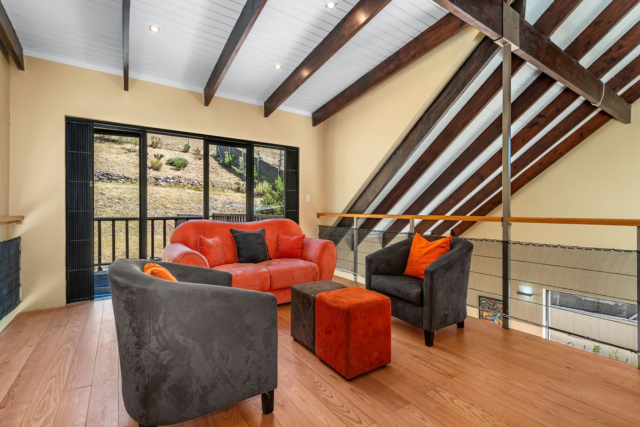 A spacious living area with a high ceiling, wooden beams, and a large sliding glass door leading to an outdoor patio.