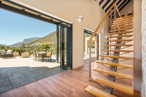 A spacious patio with outdoor furniture, a wooden staircase, and a glass door leading to a scenic view. - Houtbay Hilltop Villa (Cape Town)