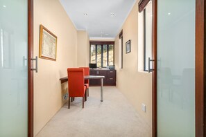 A narrow hallway with a dining area featuring a red chair and a table, a kitchen area with cabinets, and a large window providing a view of the outdoors. - Houtbay Hilltop Villa (Cape Town)