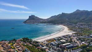 Luftaufnahme einer Küstenstadt mit Strand, Bergen und blauem Himmel.