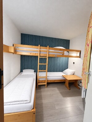 Ein kleines Zimmer mit Etagenbetten, einer Holzleiter, einem kleinen Nachttisch und einem Vorhang.