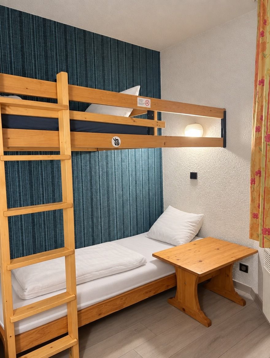 Ein Stockbett mit Holzlade, ein kleiner Holztisch und ein weißes Kopfkissen.