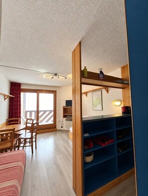 Ein Zimmer mit einem Holztisch, Stühlen, einem Bett mit gestreifter Bettdecke, einer blauen Regaleinheit und einer Schiebetür zum Außenbereich.