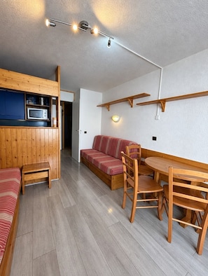A compact living space with a kitchenette, a sofa, a dining table with chairs, and a wooden bench. - Val Thorens - Ski In/Out - 5 Beds Flat (P-408) (Les Belleville)