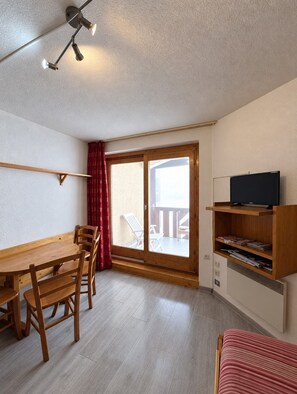A room with a wooden dining table, chairs, a television on a wooden stand, and a sliding glass door leading to an outdoor area. - Val Thorens - Ski In/Out - 5 Beds Flat (P-408) (Les Belleville)