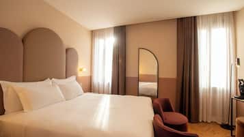 A hotel room with a large bed, a chair, a desk, and a mirror.