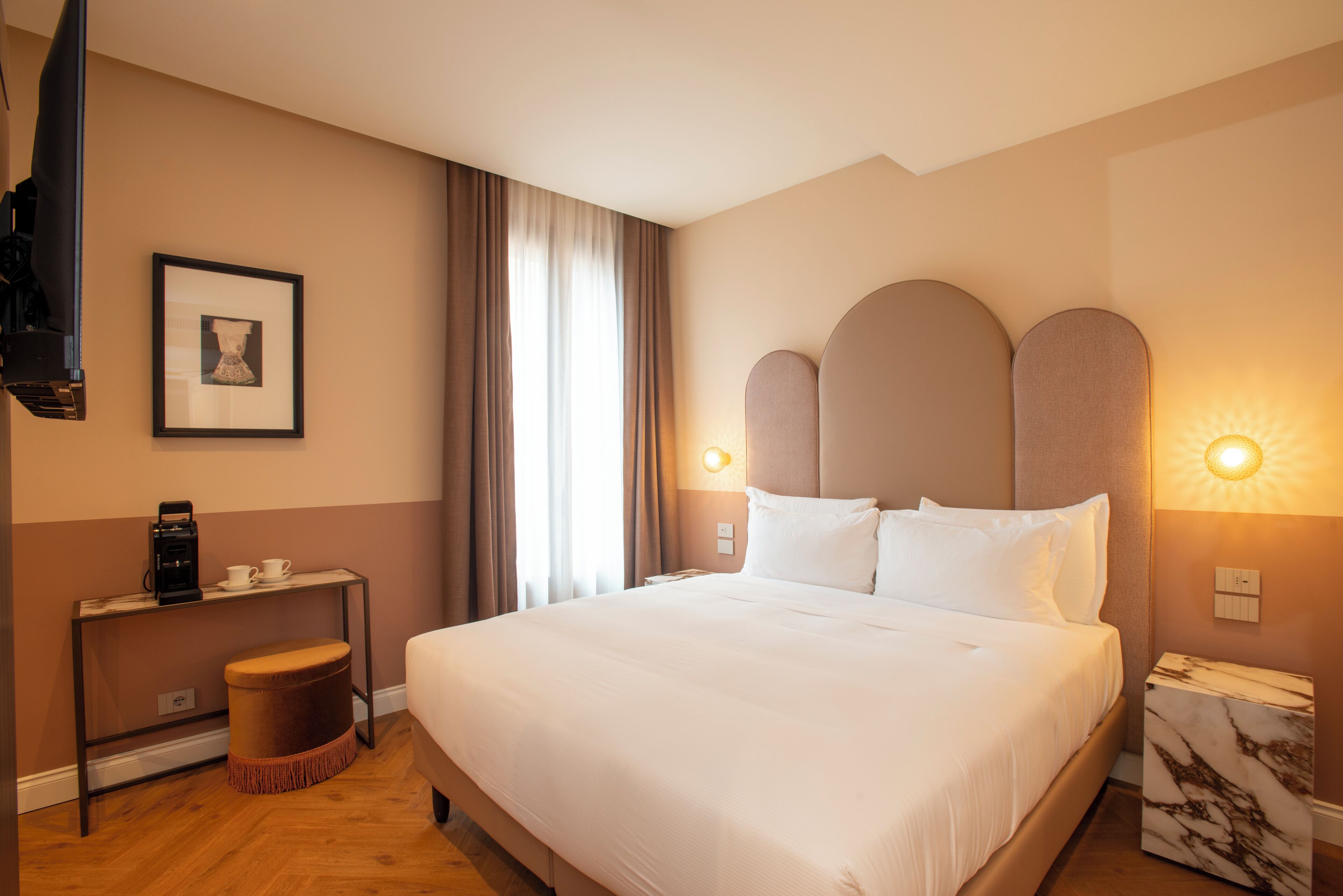 A neatly arranged hotel room with a large bed, a side table with a coffee maker, a framed picture on the wall, and a nightstand with a lamp.