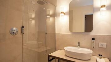 A modern bathroom with a glass-enclosed shower, a round sink, and a mirror with wall sconces.