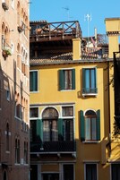 Un edificio de varios pisos con ventanas arqueadas y balcones, que presenta una fachada amarilla y contraventanas verdes.