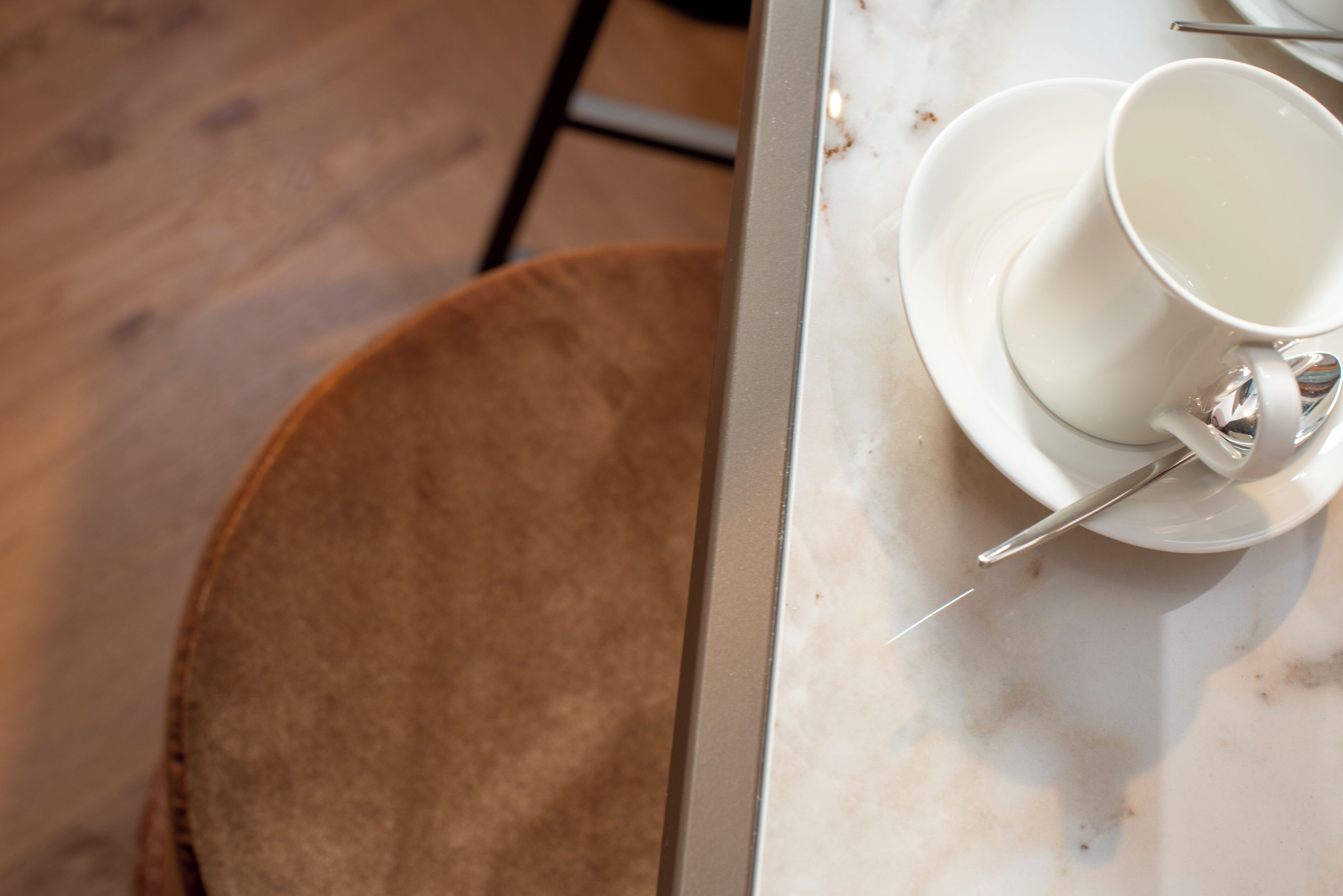 A table with a white cup and saucer, a spoon, and a brown chair.