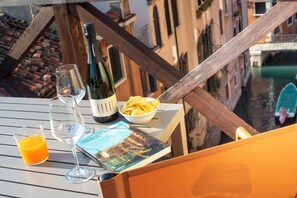 A table with a wine bottle, glasses, a bowl of chips, and a book on a balcony overlooking a canal. - Hotel de l'Alboro (Venice)