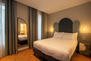 Letto rifatto con cura in una camera d'hotel, con uno specchio grande, tende e luci a parete.