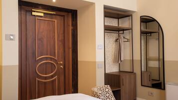 A hotel room with a wooden door, a bed, a wardrobe, a mirror, and a towel rack.