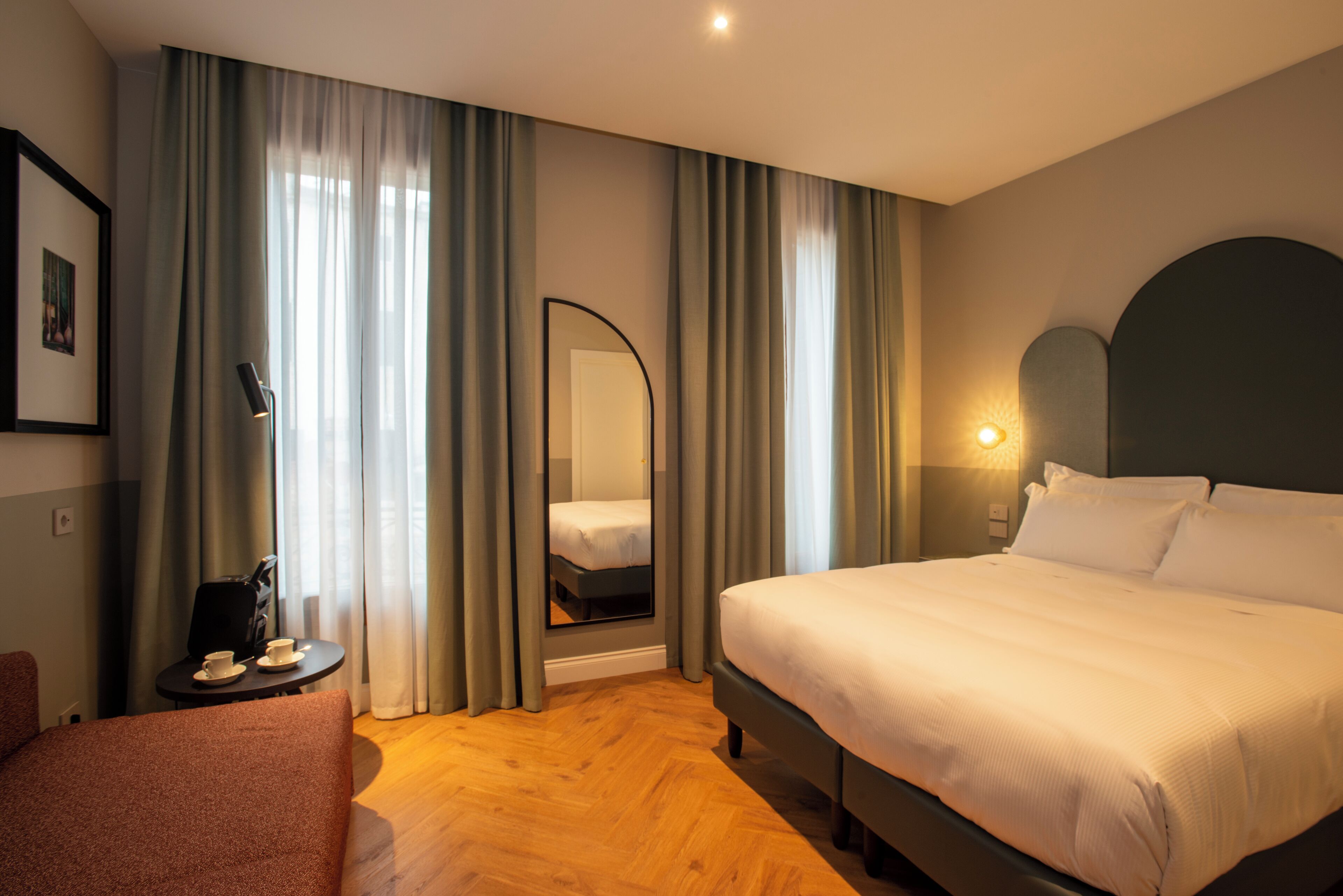 A hotel room with a large bed, a bedside table with a lamp, a chair, and a mirror.