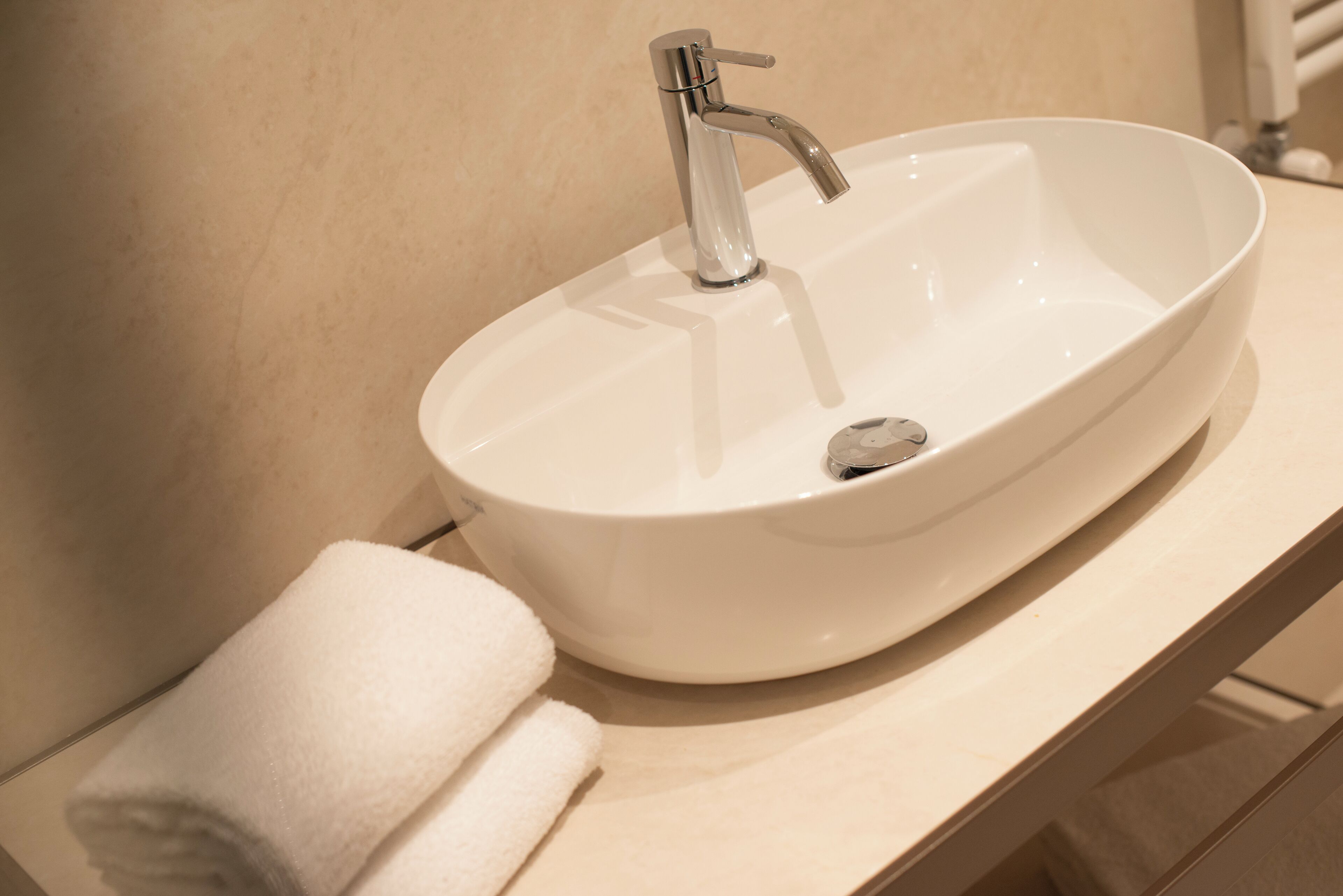 A white ceramic sink with a modern faucet, a towel, and a beige countertop.