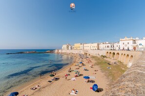 Une plage avec une eau d’un bleu limpide, des gens qui prennent des bains de soleil et des bâtiments qui bordent le rivage.