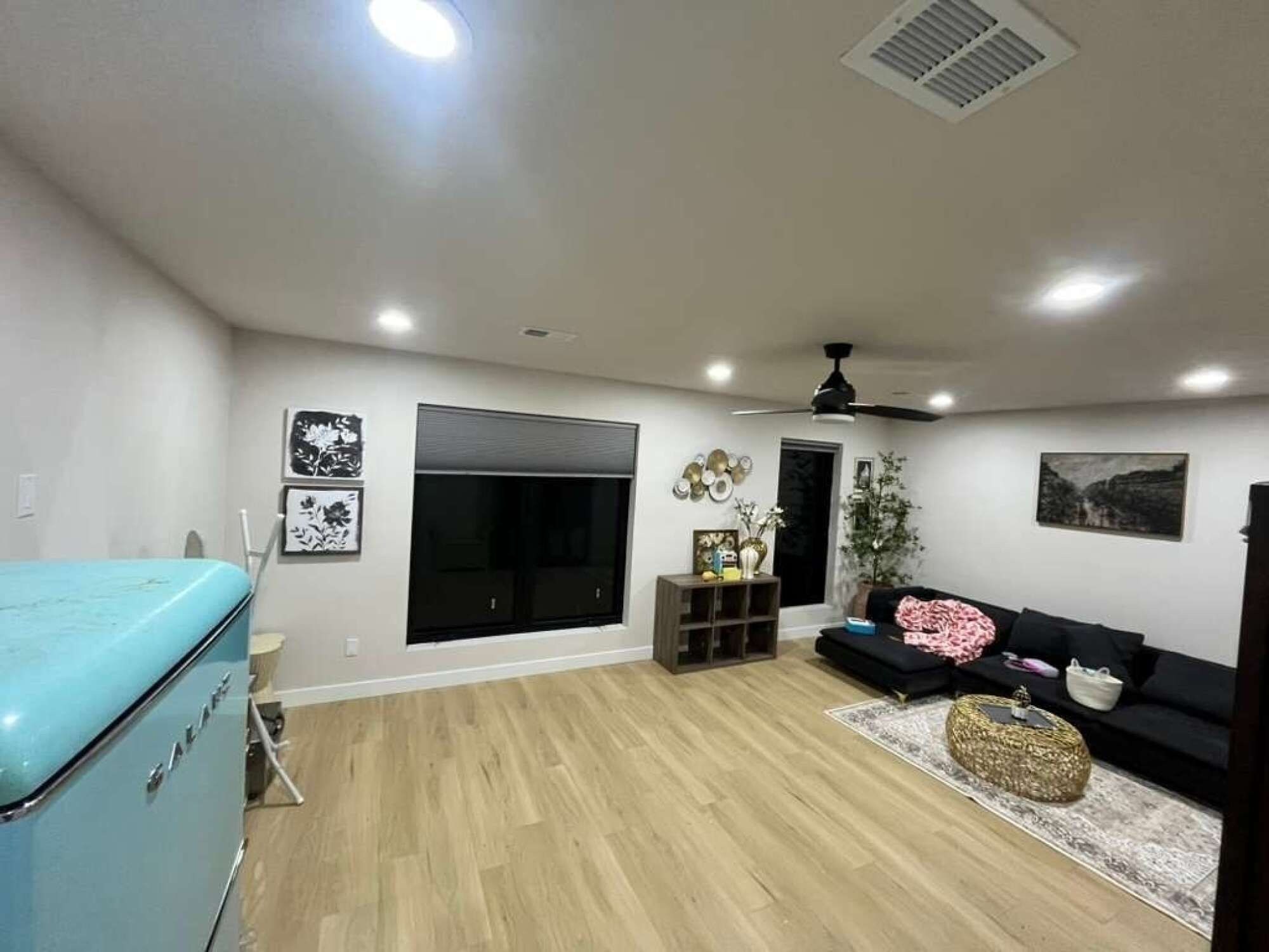 A spacious living area with a large window, a ceiling fan, and a black sofa.