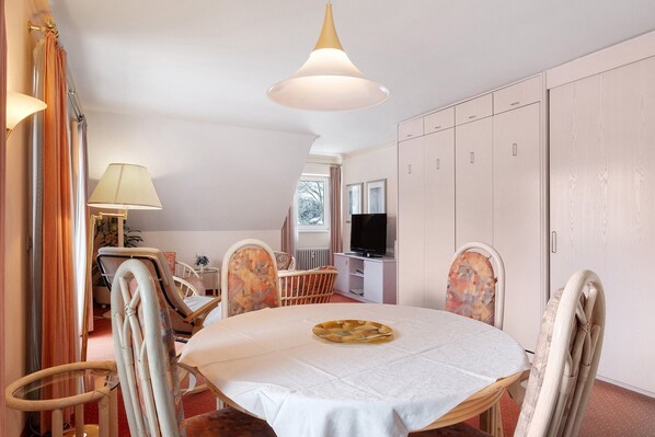 Ein Hotelzimmer mit einem runden Esstisch, Stühlen, einem Fernseher und einem Kleiderschrank.