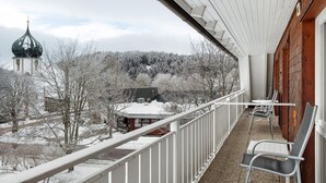 En balkon med udsigt over et snedækket landskab, en kirke med en kuppel og en bygning med rødt tag.