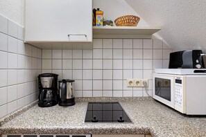 Una cocina con armarios blancos, microondas, cafetera y estufa integrada.